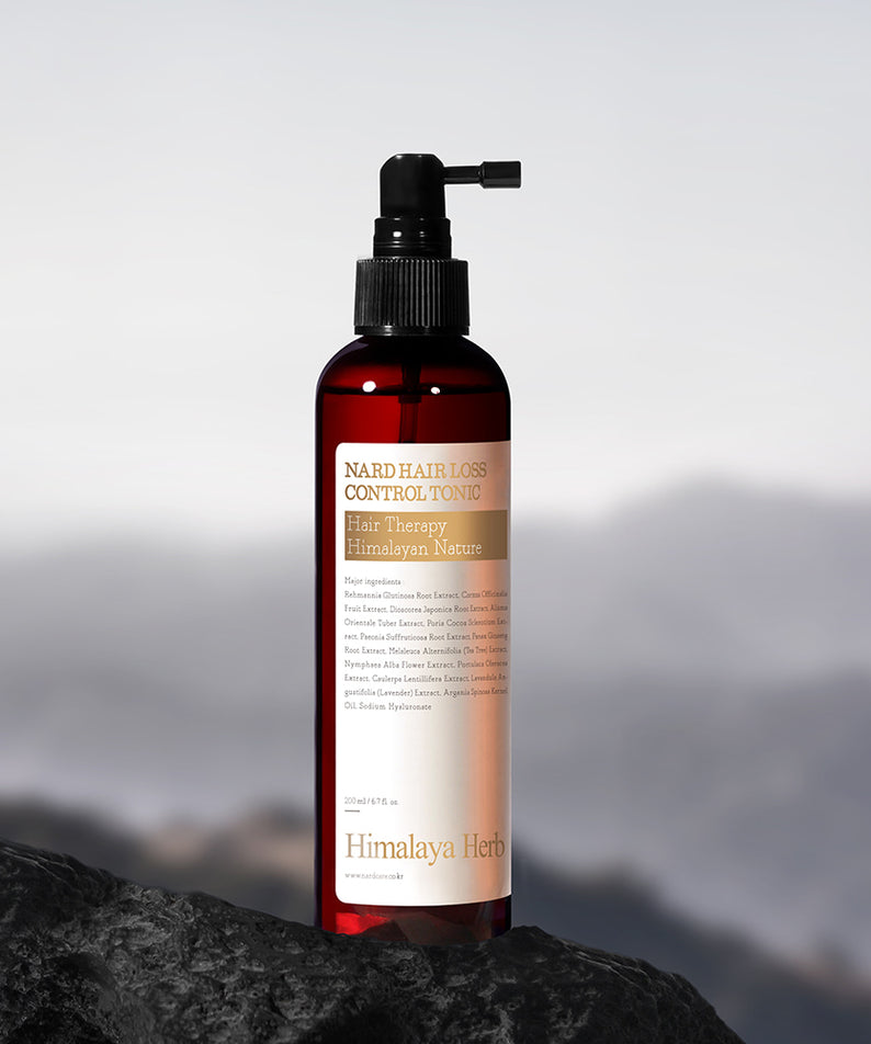 NARD Hair Loss Relief Hair Tonic 200ml de la marque NARD, flacon rouge sur rocher avec montagnes en arrière-plan.