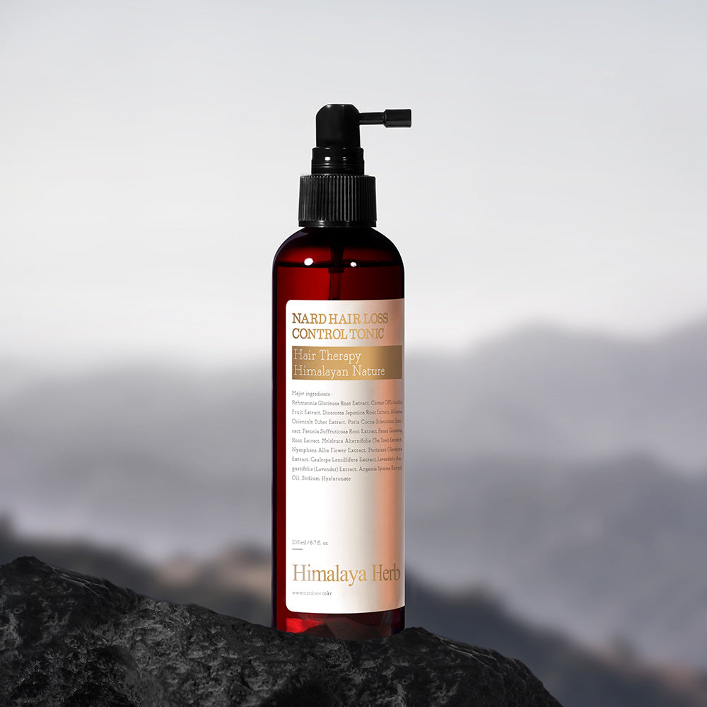 NARD Hair Loss Relief Hair Tonic 200ml de la marque NARD, flacon rouge sur rocher avec montagnes en arrière-plan.