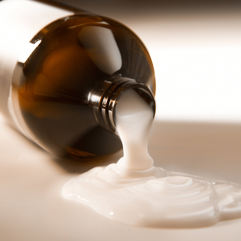 Décris l'image en français : NARD Hair Treatment 1000ml, produit de la marque NARD, flacon verseur sur texture crème blanche.