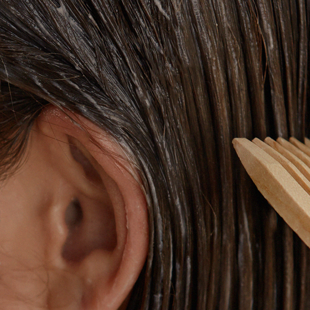 NARD Hair Treatment 1000ml, flacon de marque NARD, posé sur cheveux foncés et peigne en bois, contexte salon.