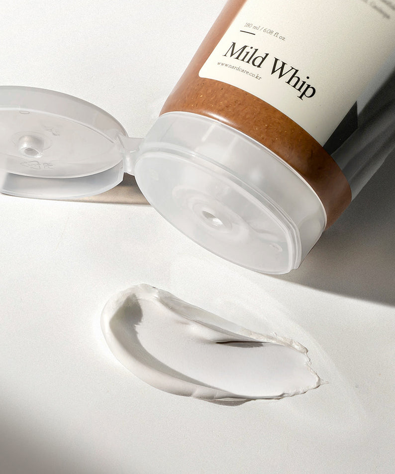 Décris l'image en français : NARD Mild Whip Pore Cleansing Foam 180ml, marque NARD, mousse sur fond blanc, flacon ouvert.