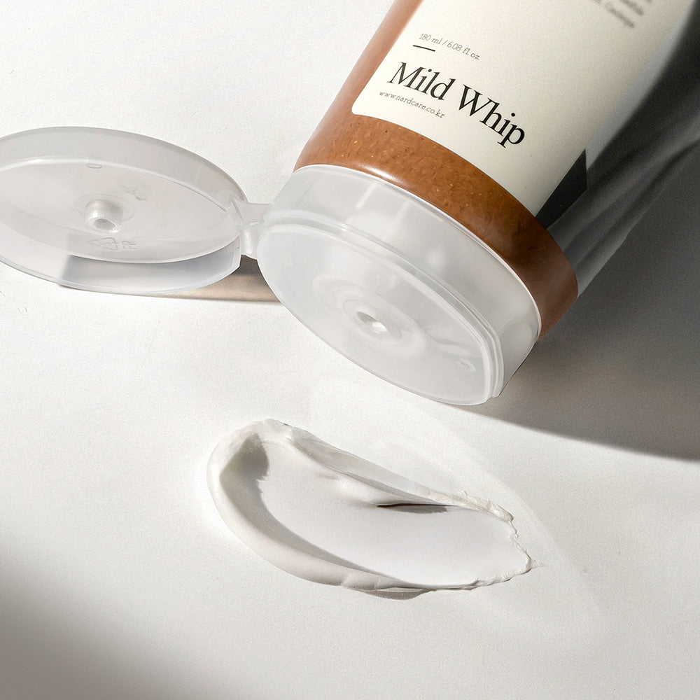 Décris l'image en français : NARD Mild Whip Pore Cleansing Foam 180ml, marque NARD, mousse sur fond blanc, flacon ouvert.