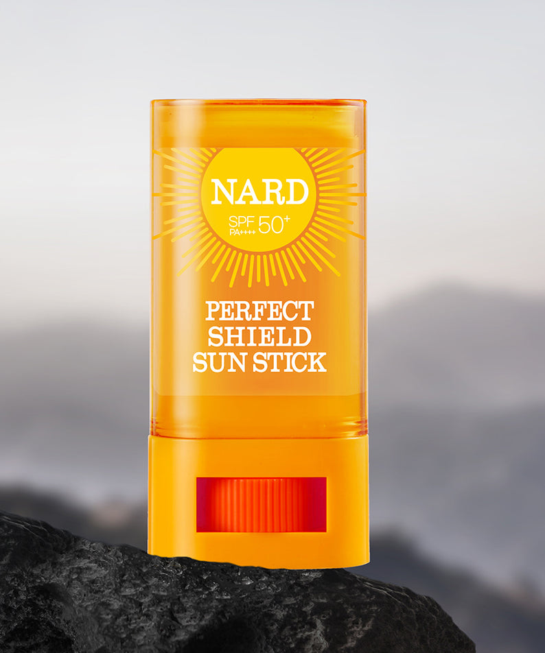 NARD Perfect Shield Sun Stick 22g de NARD, stick solaire SPF50 sur une pierre face aux montagnes, ciel en arrière-plan