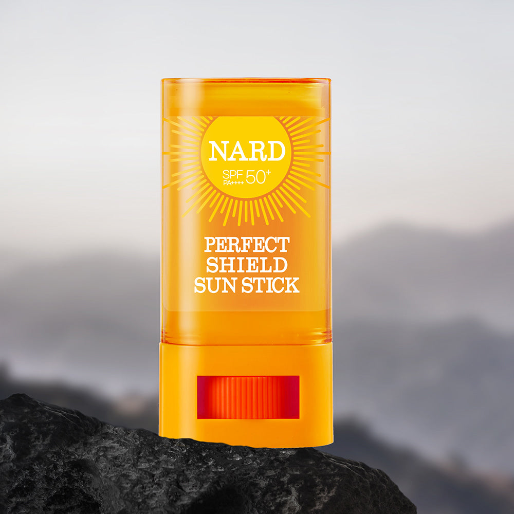 NARD Perfect Shield Sun Stick 22g de NARD, stick solaire SPF50 sur une pierre face aux montagnes, ciel en arrière-plan