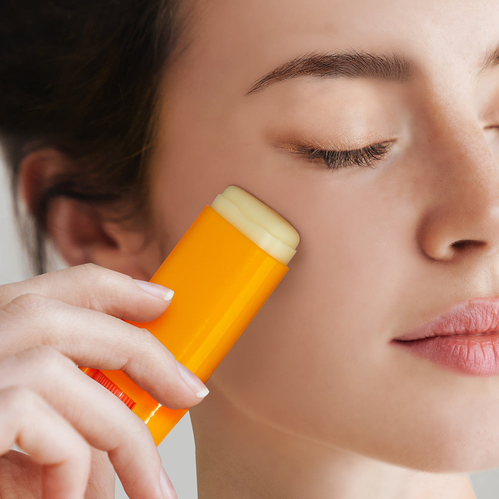 NARD Perfect Shield Sun Stick 22g, femme applique un stick solaire NARD en gros plan sur la peau, fond clair.