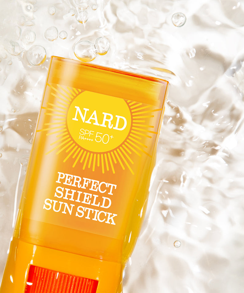 NARD Perfect Shield Sun Stick 22g, stick solaire SPF50+ jaune sur fond crème avec bulles, contexte skincare.