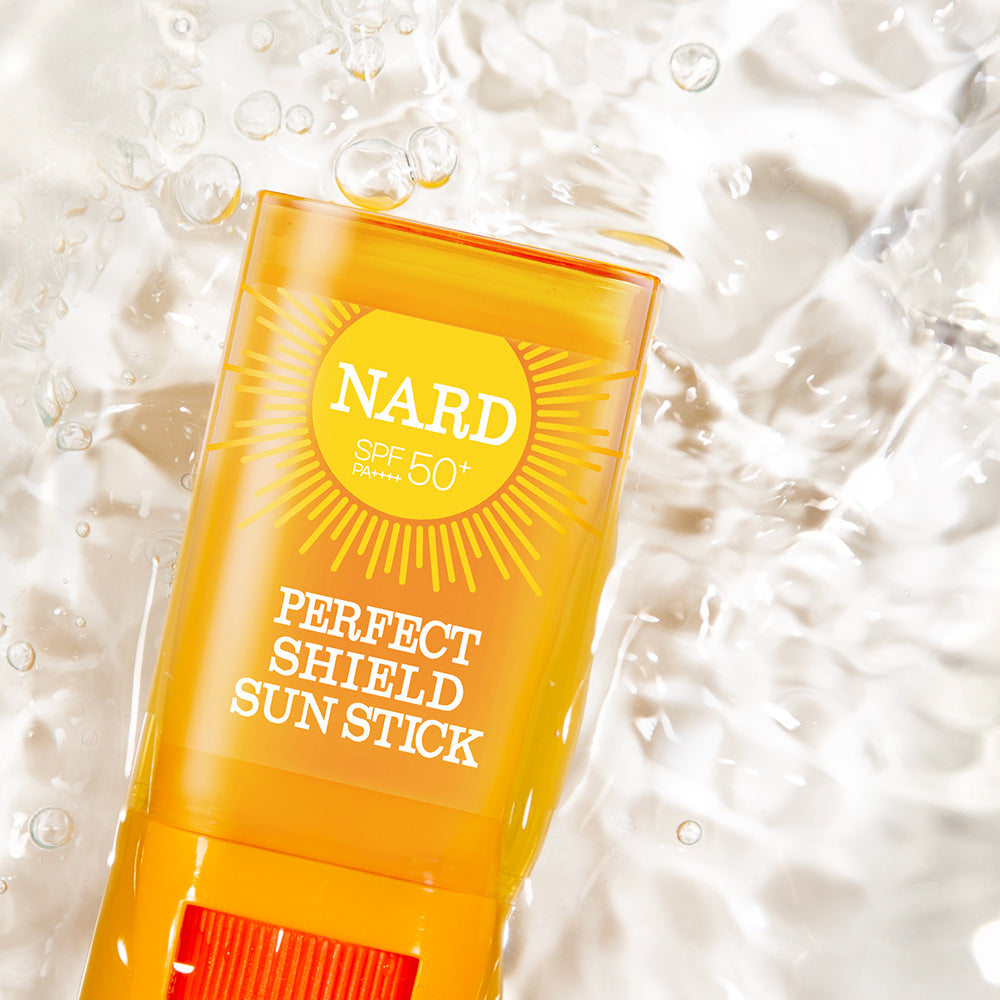 NARD Perfect Shield Sun Stick 22g, stick solaire SPF50+ jaune sur fond crème avec bulles, contexte skincare.