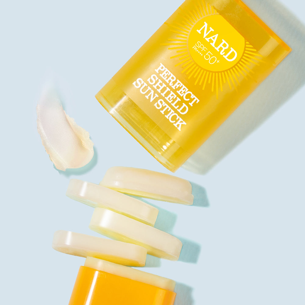 NARD Perfect Shield Sun Stick 22g de NARD, stick solaire jaune sur fond bleu clair, texture crème visible.