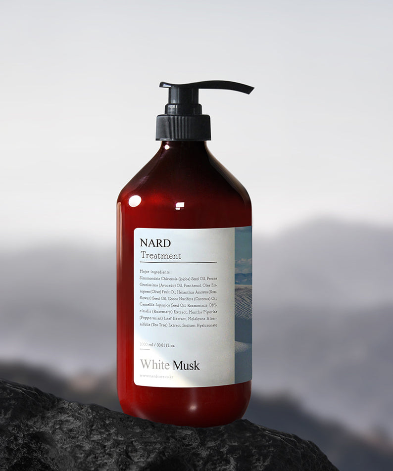 NARD Repairing Perfumed Treatment 1000ml de NARD, flacon noir pompe sur roche, parfum White Musk, fond montagnes flou.