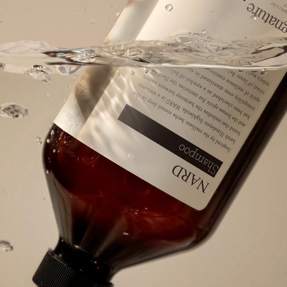 NARD Signature Shampoo 500ml de la marque NARD, flacon en plastique brun dans un bain moussant, fond clair.