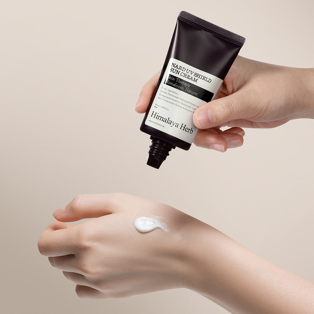NARD UV Shield Sunscreen 50ml de NARD, main appliquant la crème solaire sur la peau, contexte studio