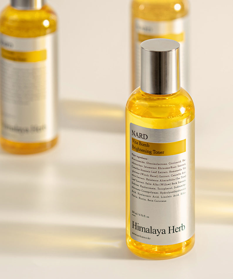 Décris l'image en français : NARD Vita Balm Brightening Toner 200ml NARD, flacon jaune avec lumière douce en arrière-plan.