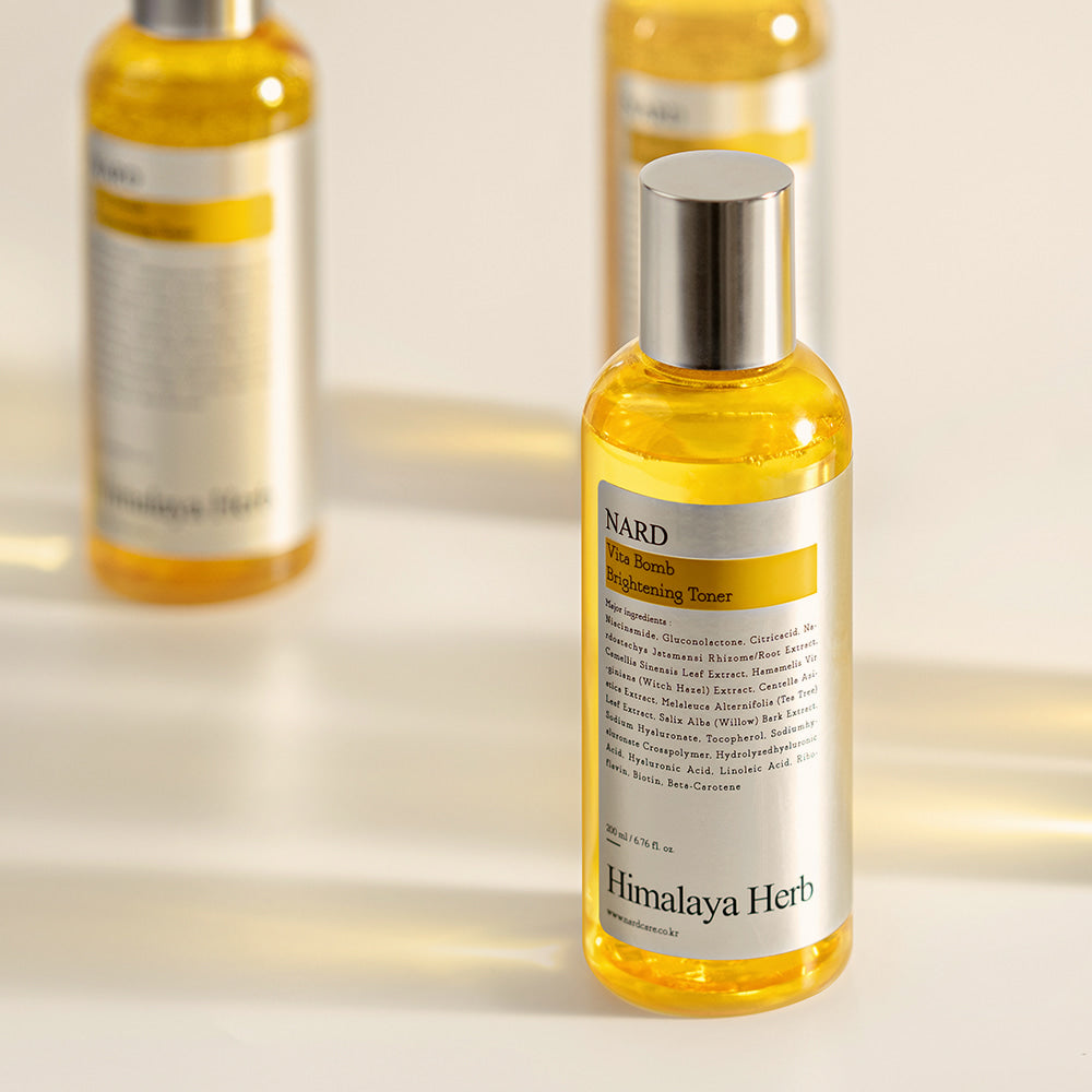Décris l'image en français : NARD Vita Balm Brightening Toner 200ml NARD, flacon jaune avec lumière douce en arrière-plan.
