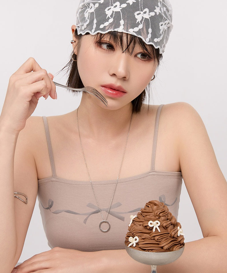 Femme avec dessert au chocolat, portant un haut beige et un bandana en dentelle, posant pensivement assise.