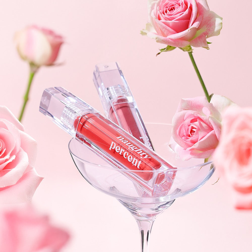 NAUGHTY PERCENT Matte Bloom Tint de la marque NAUGHTY PERCENT, rouge à lèvres mat, présenté dans un verre avec roses roses.