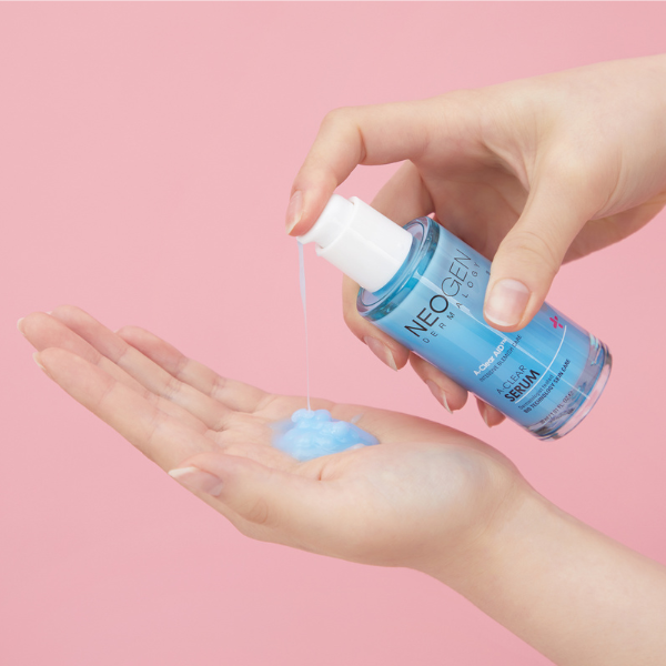 NEOGEN A Clear Serum 30ml de NEOGEN, main versant un sérum bleu sur la peau, fond rose pastel.