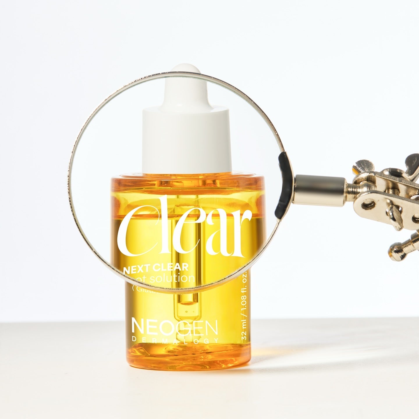 NEOGEN  Next Clear Spot Solution 32ml, flacon jaune avec loupe sur fond clair : soin anti-imperfections.
