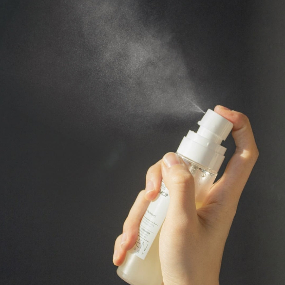 NEOGEN White Truffle Ampoule Drop Mist 80ml, main tenant le flacon, contexte beauté sur fond sombre, marque NEOGEN