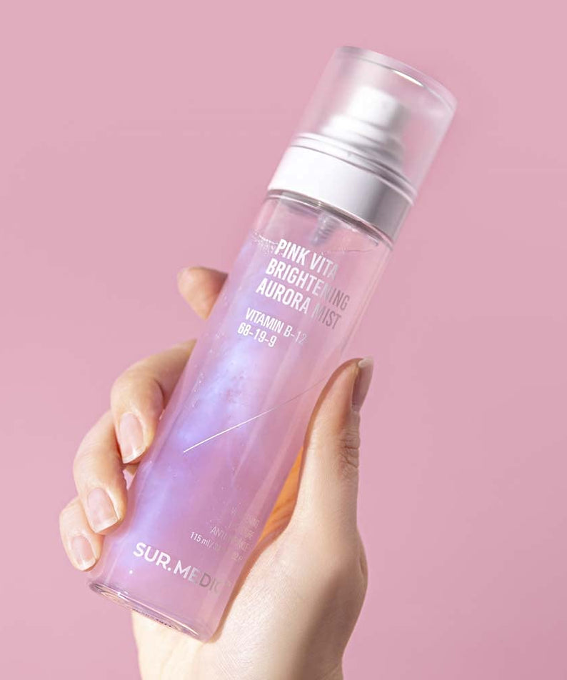 Bouteille de NEOGEN Pink Vita Aurora Mist 115ml tenue à la main sur fond rose, soin visage hydratant et éclatant.