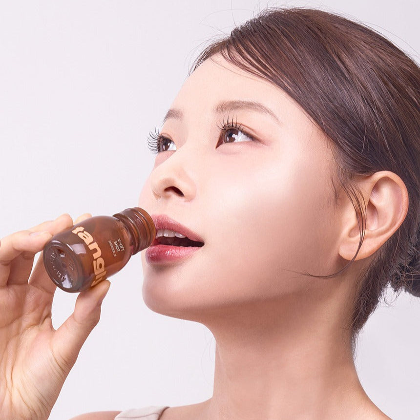 Décris l'image en français : NOTHING BETTER Tangly V-Life Shot 7 Bottles, marque, femme boit un shot, fond clair.