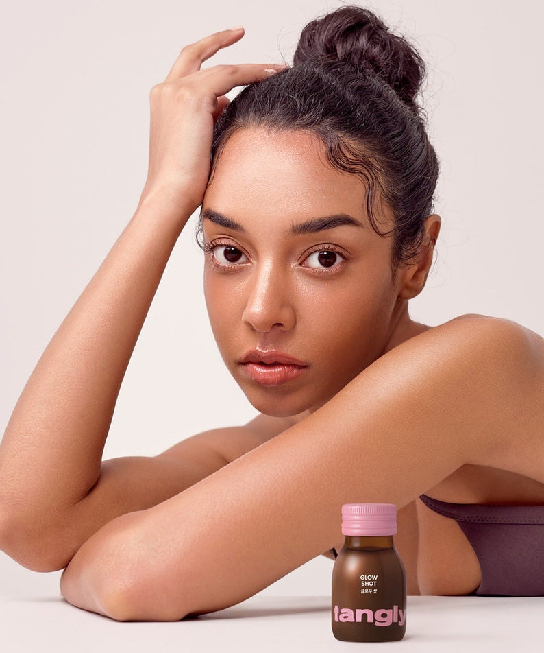 Femme posant avec bouteille de NOTHING BETTER Tangly Glow Shot. Découvrez la beauté naturelle avec 7 bouteilles du booster d'éclat.