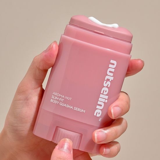 NUTSELINE Aroma Nut Slim Fit Body Guasha Serum 60ml, flacon rose tenu en main, contexte visuel beauté spa sur fond clair.