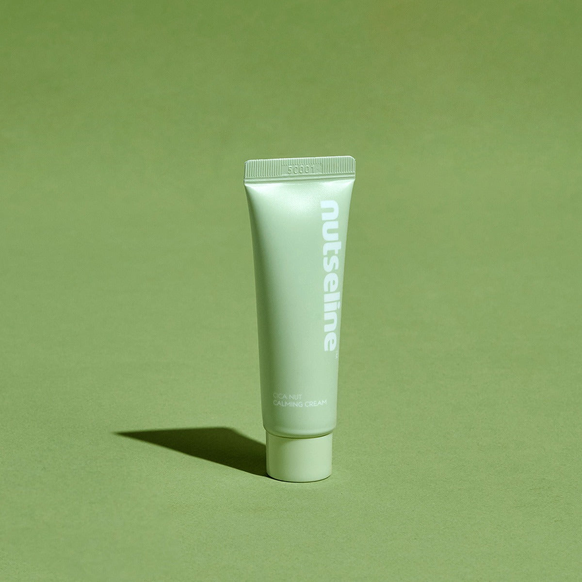 Décris l'image en français : NUTSELINE Cica Nut Calming Cream 25ml, tube vert de la marque NUTSELINE sur fond vert.
