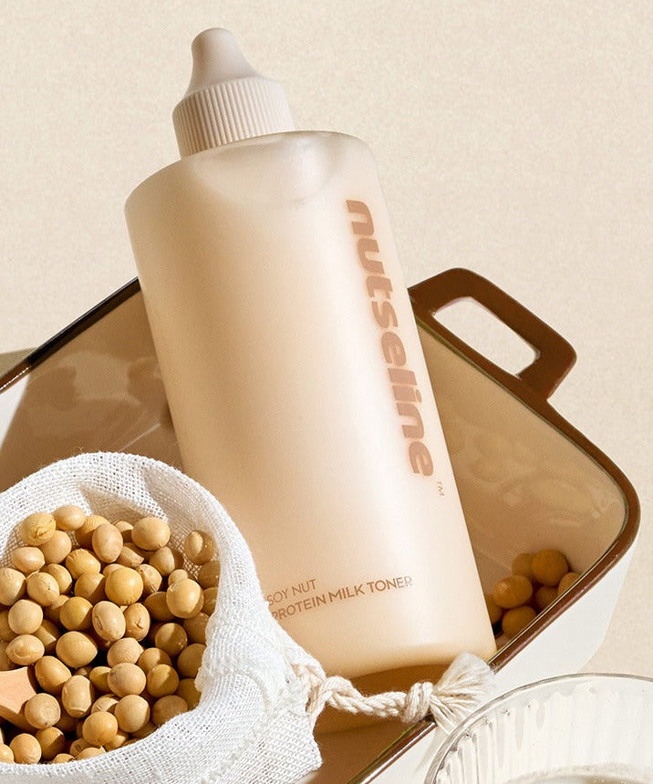 NUTSELINE Soy Nut Protein Milk Toner 300ml : flacon beige sur fond neutre avec sachet de soja et accessoires visuels.