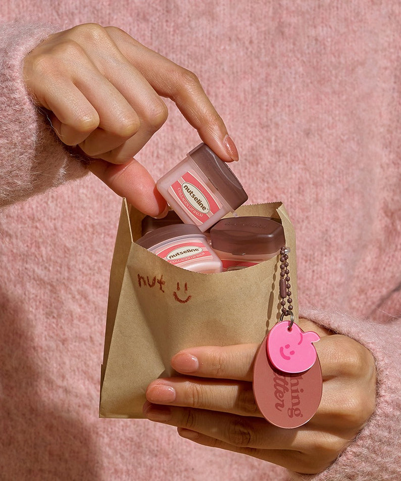 Décris l'image en français en mentionnant le produit, la marque et le contexte visuel : NUTSELINE Super Nut Collagen Keyring Lip Balm 11ml