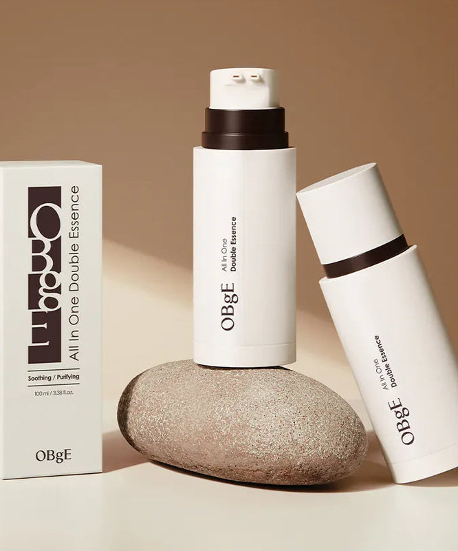 OBGE All-in-one double essence 100ml, flacon crème et boîte OBGE sur fond beige, style cosmétique minimaliste.