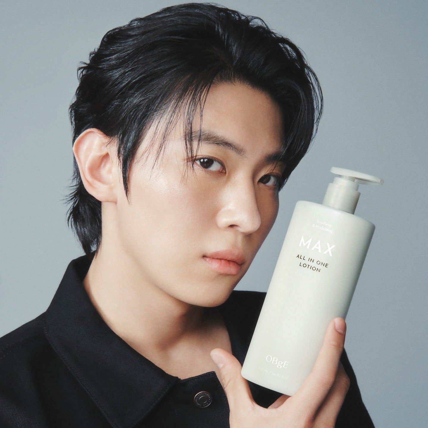 OBGE Max All-in-One Lotion 500ml : flacon crème tenu par un homme, fond bleu clair, marque OBGE visible.