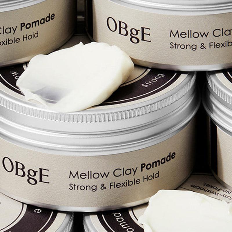 OBGE Mellow Clay Pomade 100g d’OBGE : pots de pomade à l’arrière-plan, vue rapprochée en salle de soins capillaires.