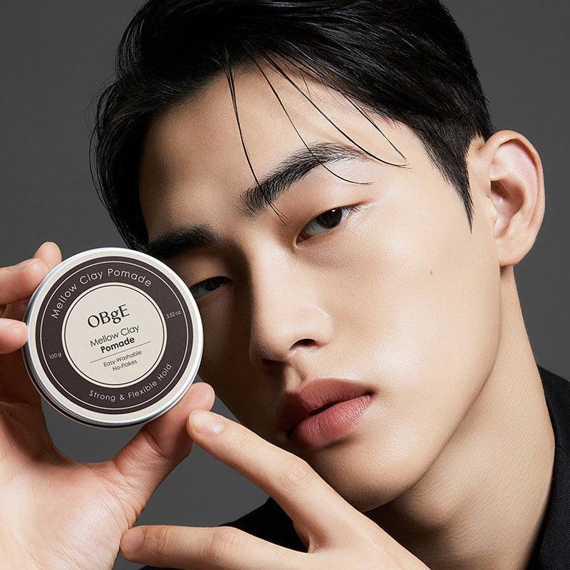 OBGE Mellow Clay Pomade 100g d’OBGE, homme tenant le pot sur fond gris, style coiffure naturel.