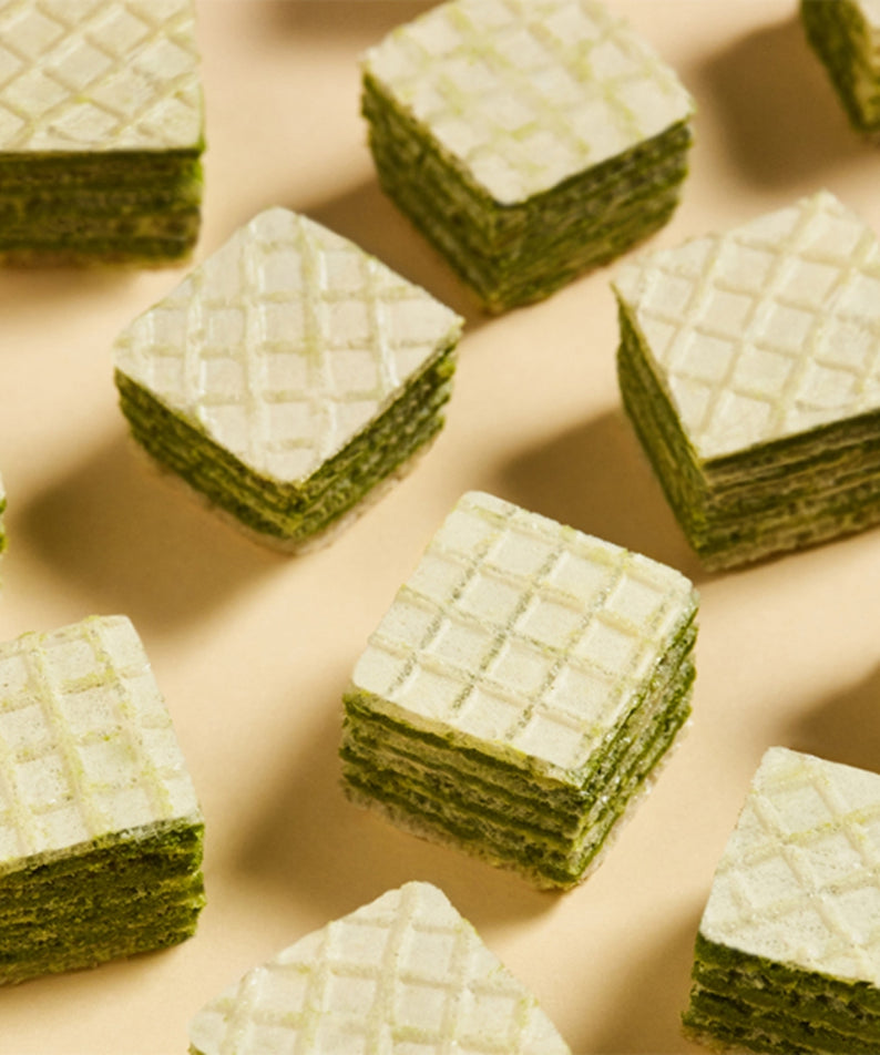 Délicieuses gaufrettes au thé vert OSULLOC Green Tea Wafers 100g, empilées en carrés sur une table, parfaites pour une pause gourmande.