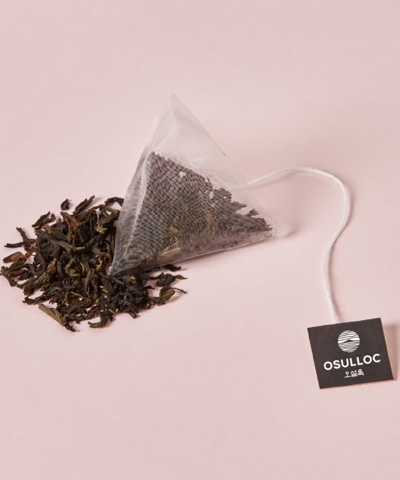 Sachet de thé OSULLOC Milky Oolong Tea 10 p avec des feuilles en vrac sur fond rose.