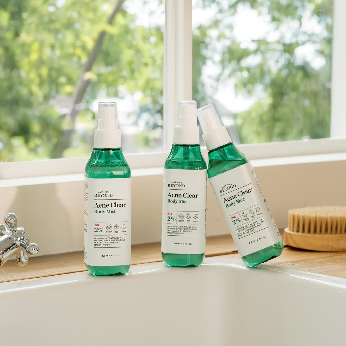 PASSON & BEYOND Acne Clear Body Mist 200ml, flacons verts sur rebord près d’une fenêtre, salle de bain lumineuse.