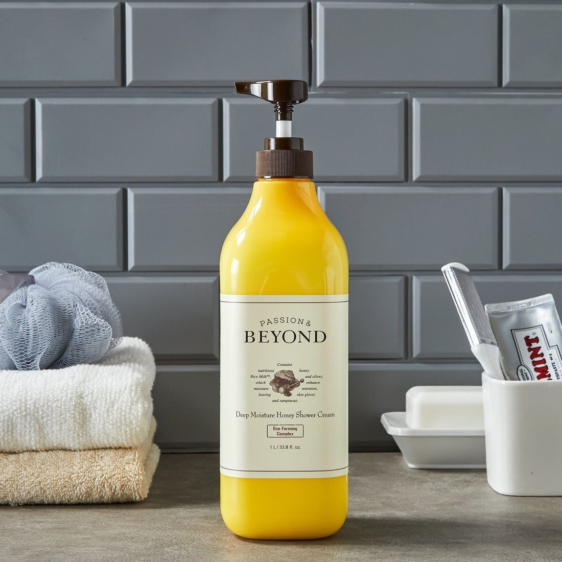 PASSON & BEYOND Deep Moisture Honey Shower 1L : bouteille miel sur planche avec serviettes, salle de bain, arrière-plan briques
