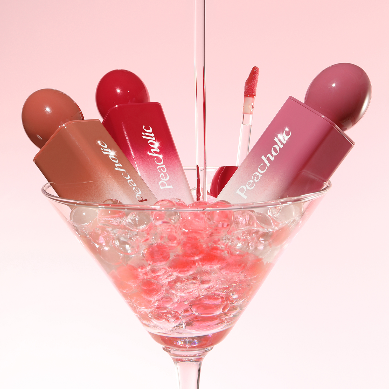 PEACHOLIC Water Glow Lip Tint de Peacholic, maquillage en gouttelettes roses, tube et gloss en flûte sur fond rose.