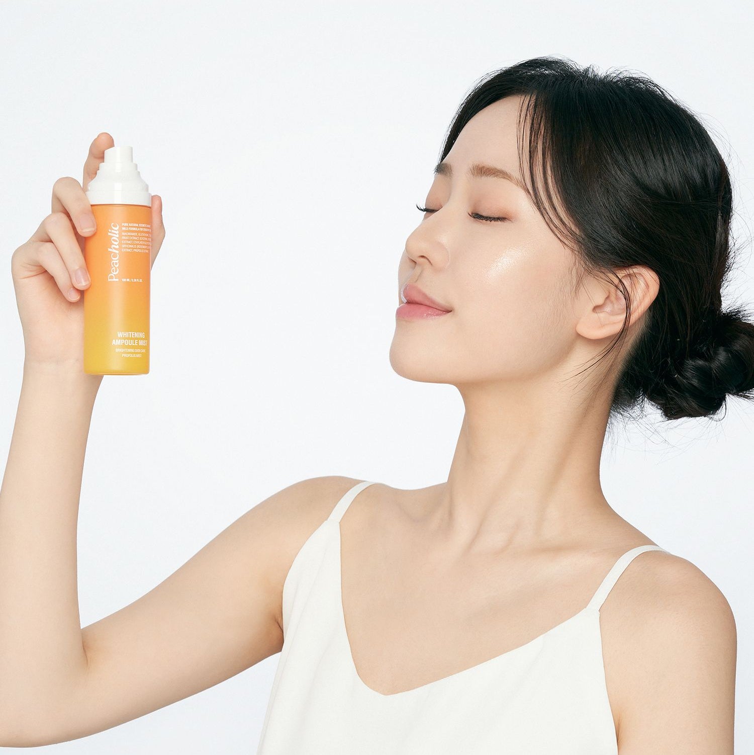 PEACHOLIC  Whitening Ampoule Mist 100ml : femme en vaporisation, flacon orange de la marque sur fond blanc, soin éclaircissant