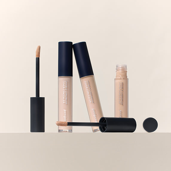 PERIPERA Double Longwear Cover Concealer, gamme de correcteurs beige; tubes et pinceau sur fond clair, style maquillage.