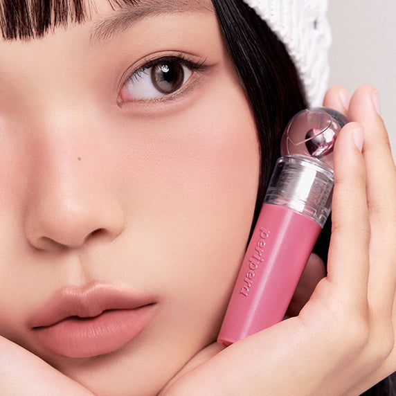 Décris l'image en français : PERIPERA Ink The Gellable Tint, la marque, lèvres et flacon sur visage maquillé, gros plan.