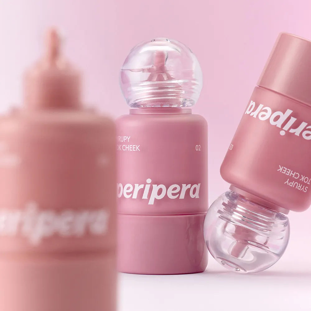 Décris l'image en français : PERIPERA Syruppy Tok Cheek, blush coréen rosé, flacons roses sur fond pastel.