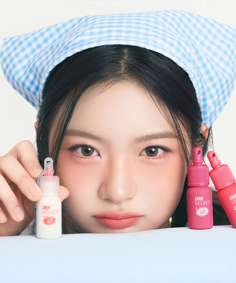 PERIPERA Ink The Velvet : maquillage lèvres, marque coréenne, femme avec bonnet bleu et flacons roses sur fond clair