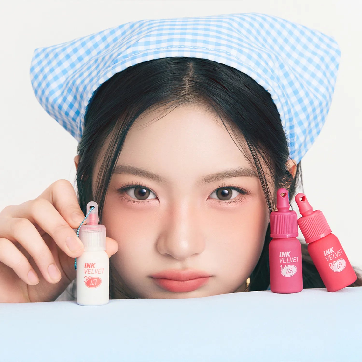PERIPERA Ink The Velvet : maquillage lèvres, marque coréenne, femme avec bonnet bleu et flacons roses sur fond clair