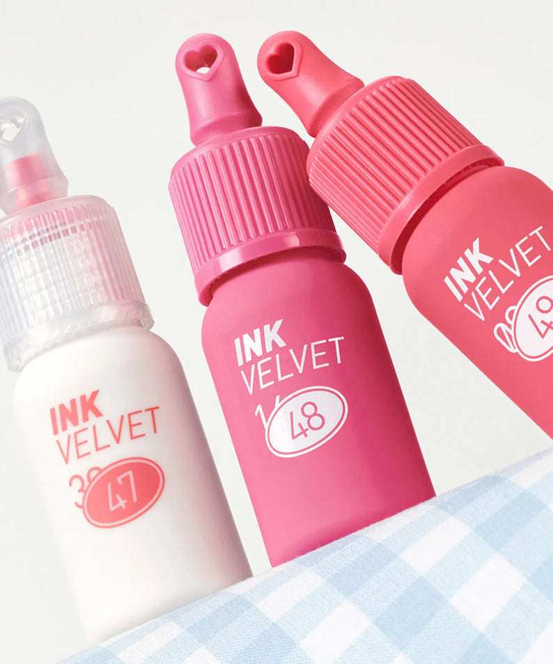 PERIPERA Ink The Velvet : flacons de maquillage rose et blanc, packshot sur tissu à carreaux, marque PERIPERA