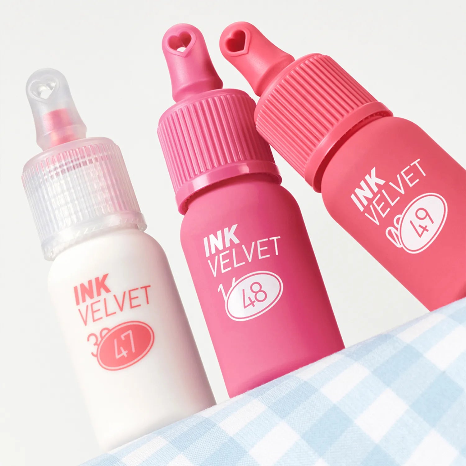 PERIPERA Ink The Velvet : flacons de maquillage rose et blanc, packshot sur tissu à carreaux, marque PERIPERA