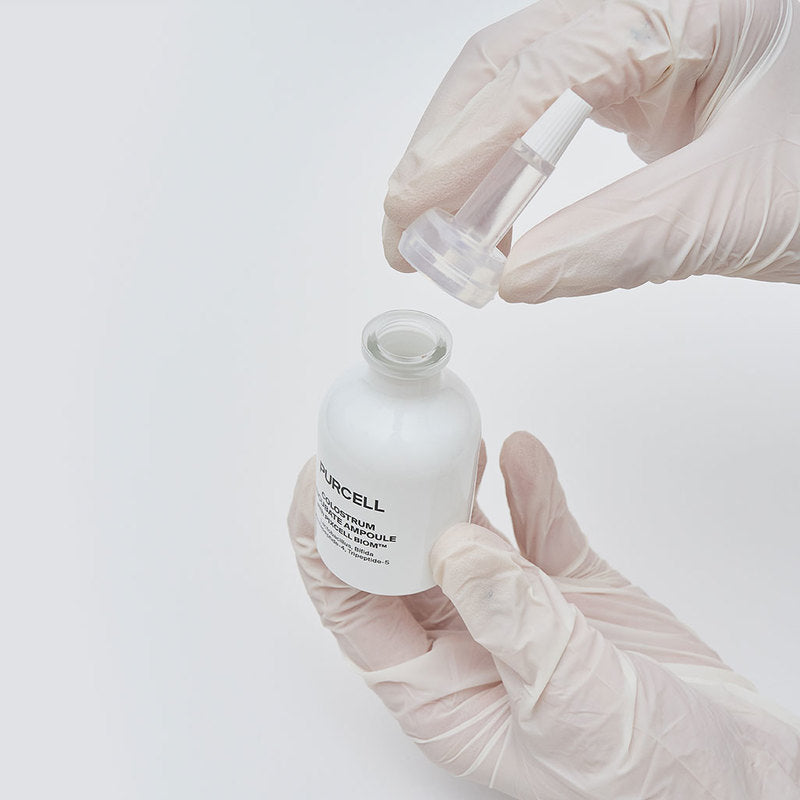 PURCELL Colostrum Incubation Ampoule 30mL de PURCELL en ampoule, mains gantées, préparation en laboratoire sur fond blanc.