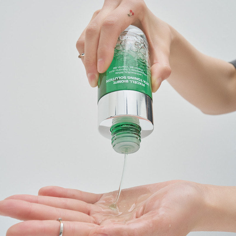 Main appliquant PURCELL PixelBiome™ Vita Toning Solution 120mL PURCELL, sur peau, flacon à pompe sur fond clair