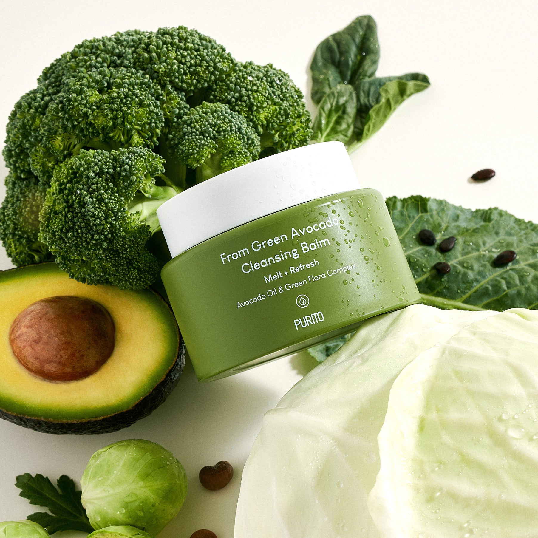 PURITO From Green Avocado Cleansing Balm 100ml : pot vert sur ingrédients verts (avocat, brocoli, feuilles), contexte spa naturel.