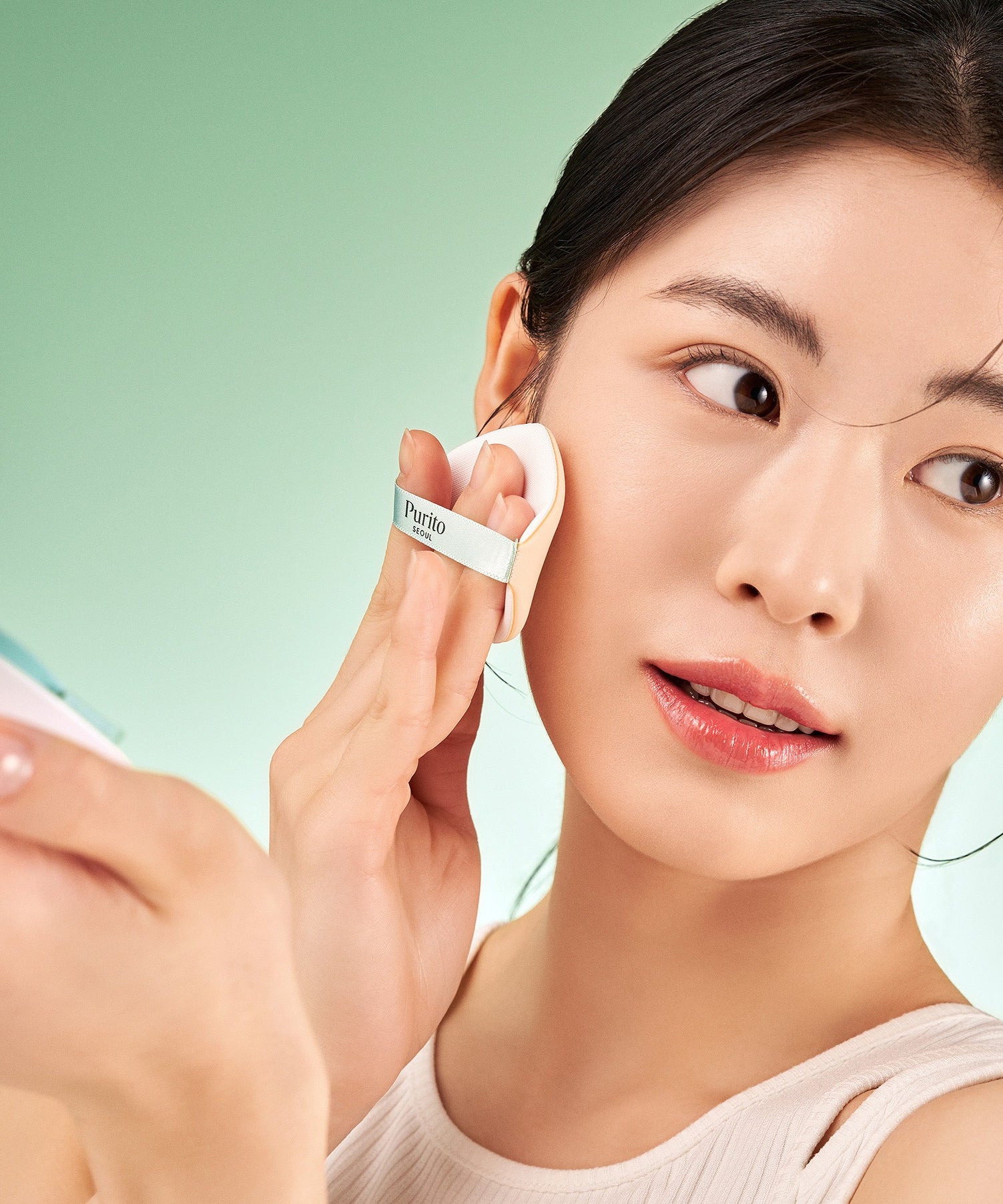 PURITO Wonder Releaf Celtella BB Cushion 15g de Purito, femme maquillage appliquant le BB en studio sur fond vert.